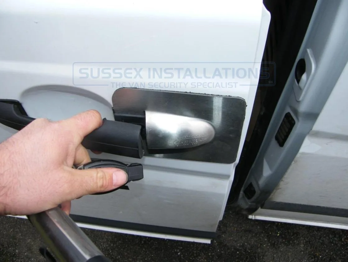 A hand fitting an Armaplate shield to a van door handle, aligning the stud with the marked position