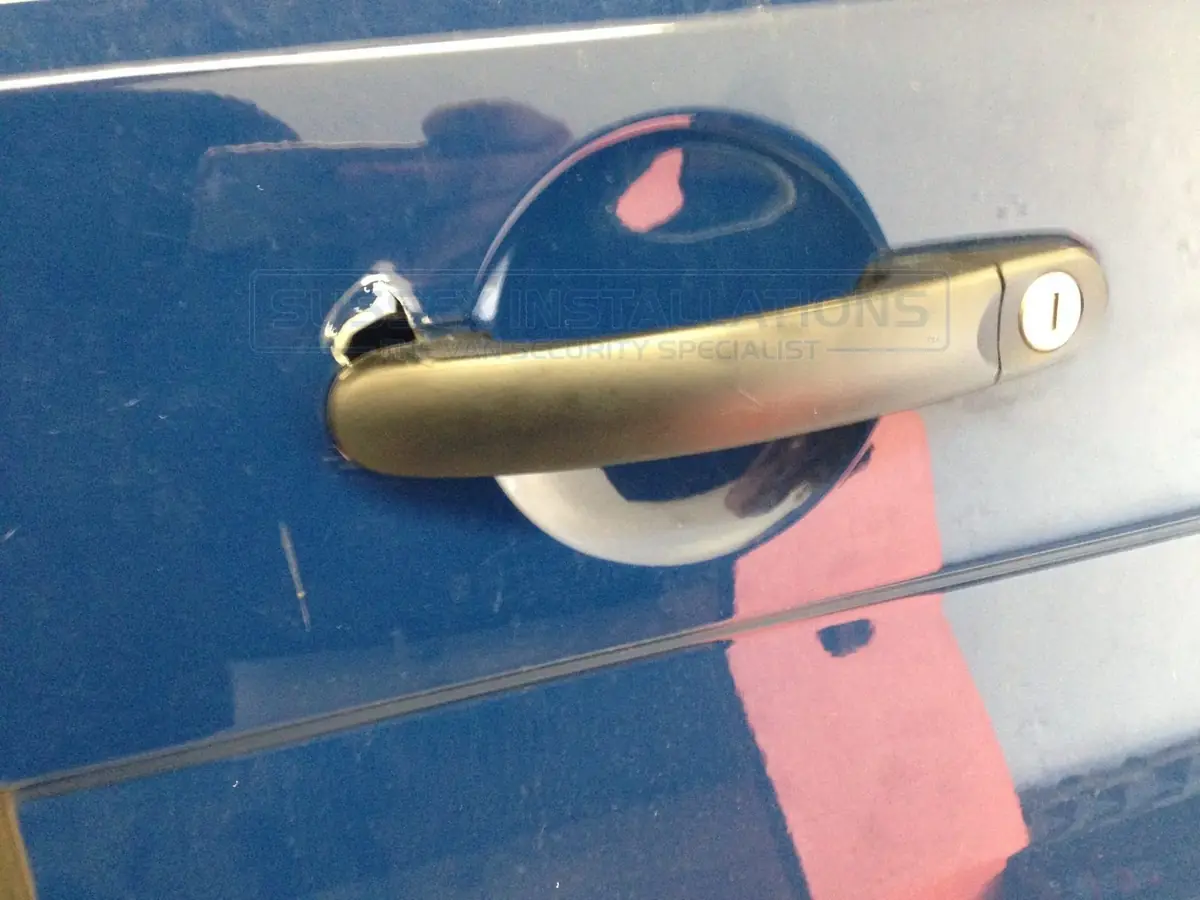 Close-up of a chipped and cracked area at the base of a van door handle, typical of an older-style screwdriver-lever attack