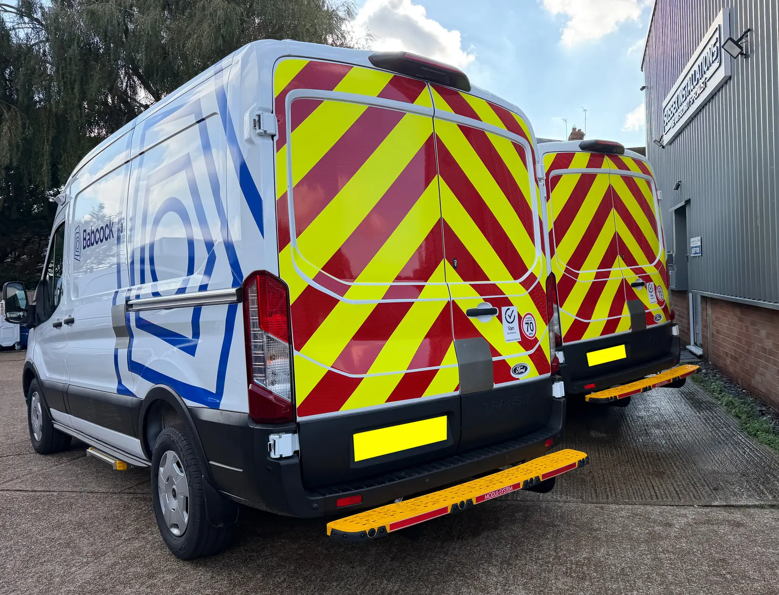 Rear of two service vans with red and yellow chevron panels at the Sussex Installations workshop