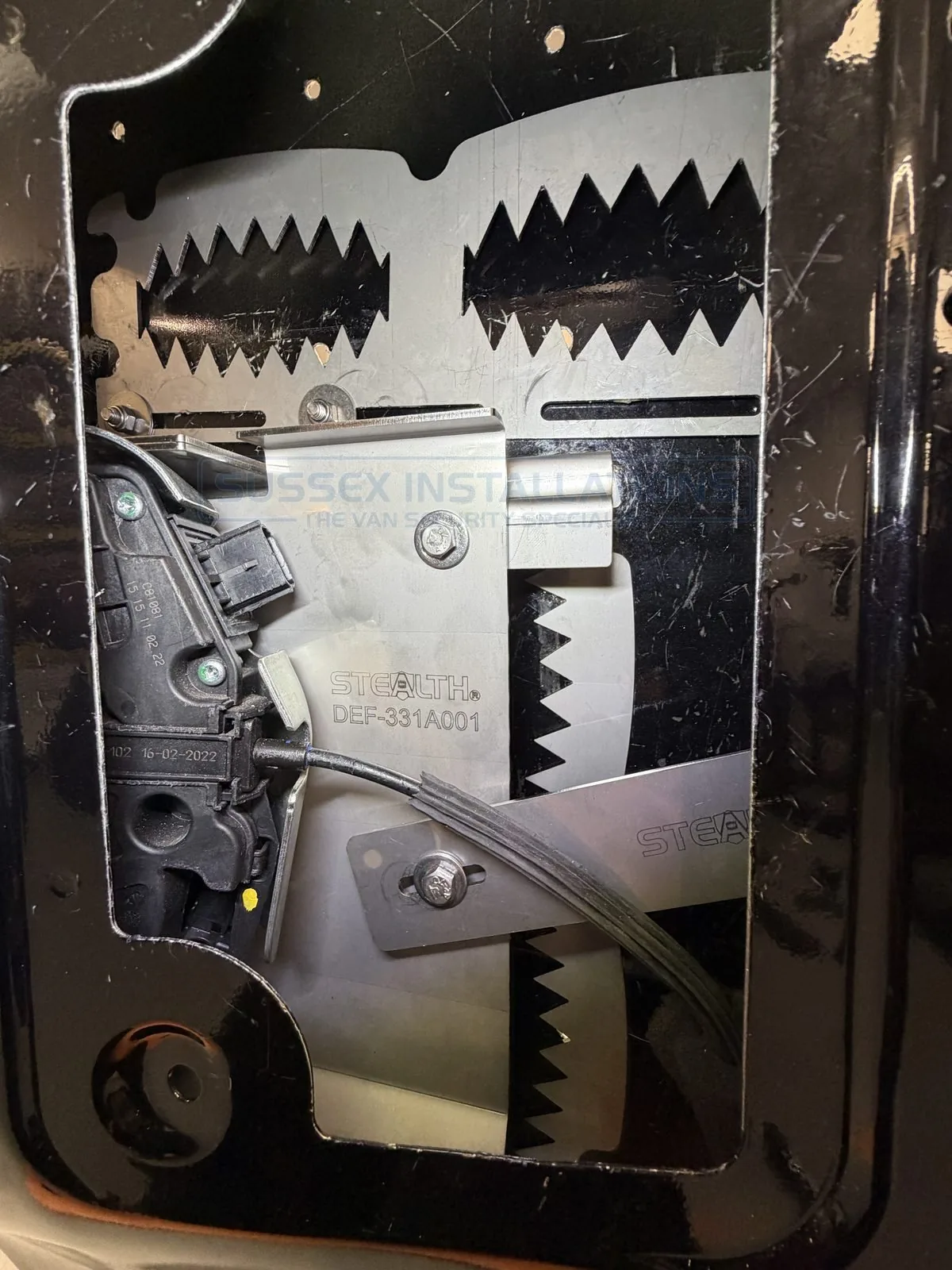 A stealth trap anchor and defender shield fitted inside a van door, illustrating the more complete internal geometry developed to resist cutting and folding attacks rather than relying on a single flat plate