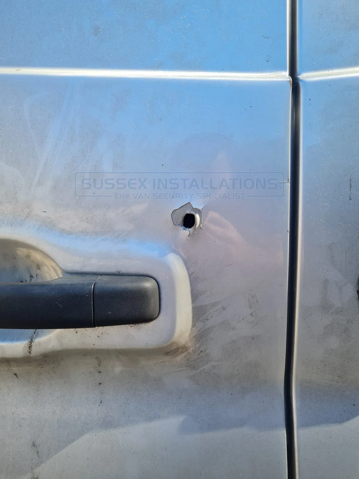 A hole cut straight through the metal skin of a van door, reaching directly for the latch, typical of the hole-through-the-door attacks that began around 2018